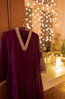 Purple dress with white lace trim hangs on a door, with warm, glowing lights in the blurred background, creating a festive and cozy ambiance.