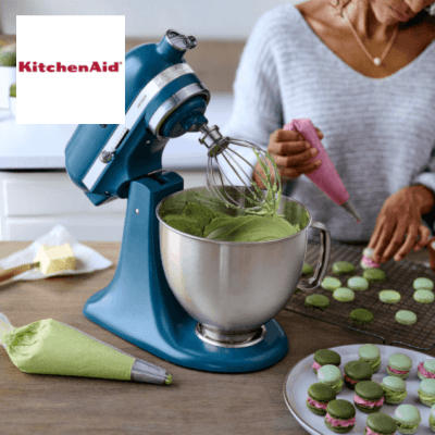 blue KitchenAid mixer on a worktop with woman icing in background