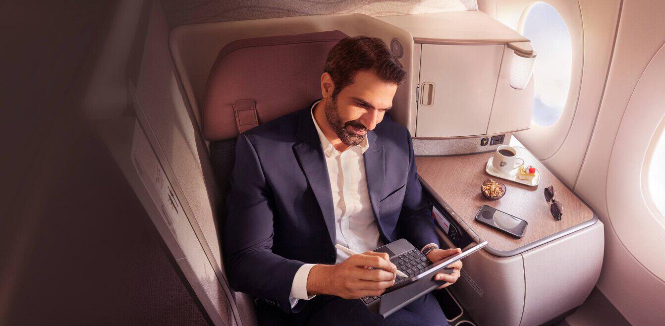 Air India deals page image showing a happy man using a tablet in a luxurious first class seat