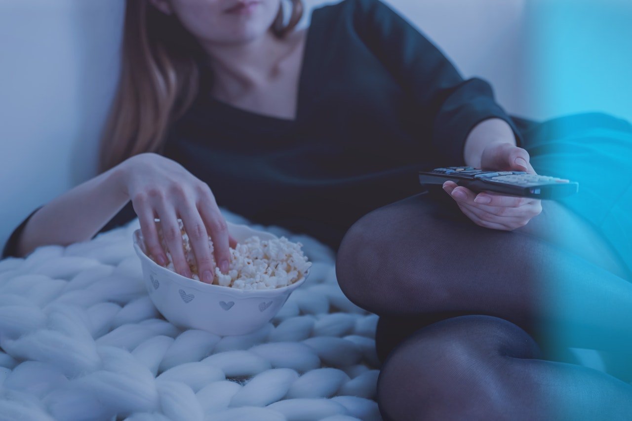 Femme qui regarde la télévision en mangeant du pop corn avec une télécomande dans les mains