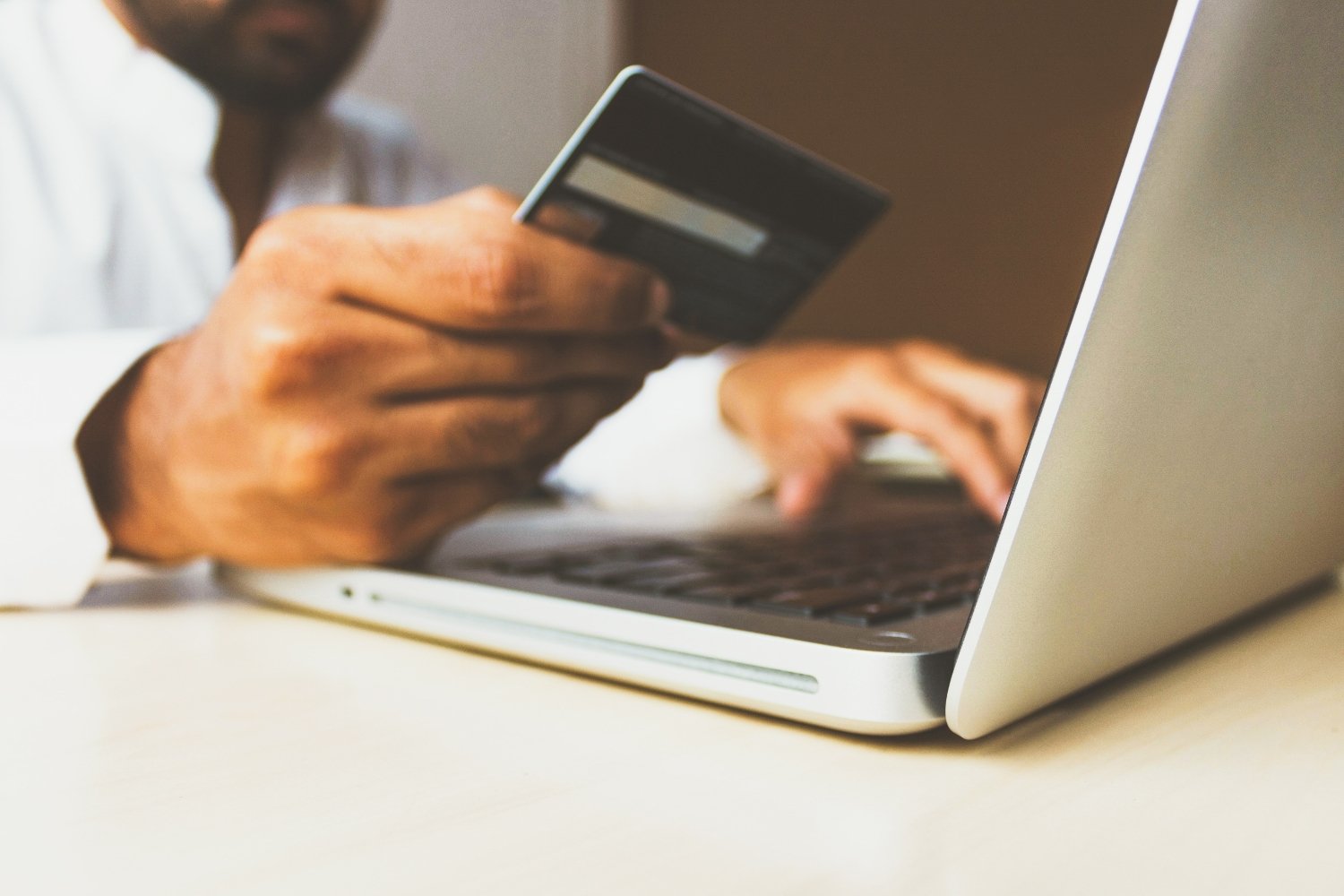 Person shoppt online am Laptop mit einer schwarzen Kreditkarte