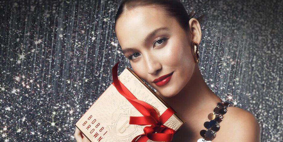 Bobbi Brown christmas banner showing a glamorous woman made up with makeup holding a gift set