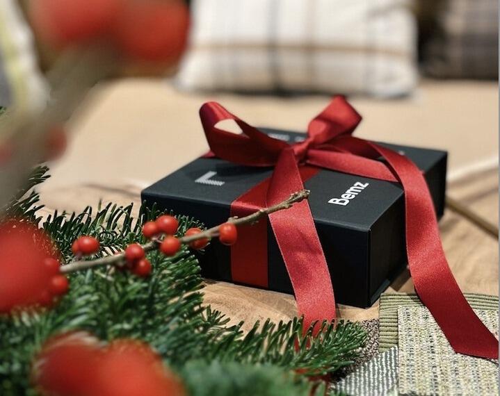 Boîte cadeau de Noël Bemz sur une table en bois avec du houx et des échantillons de tissus