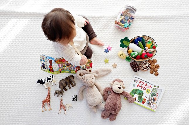 Kleinkind umringt von bunten Spielsachen, Büchern und Kuscheltieren