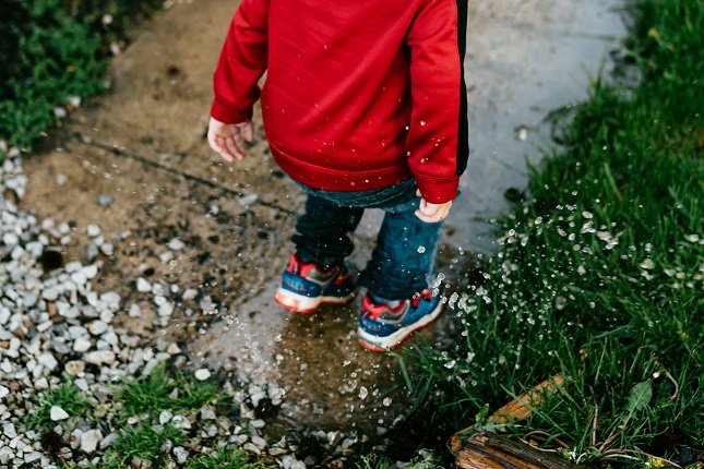 Kind in roter Jacke springt draußen in eine Pfütze