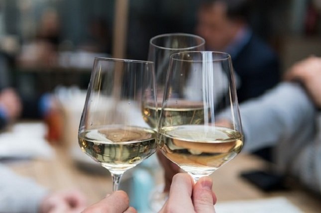 Drei Gläser halb gefüllt mit Weißwein werden zum Anstoßen zusammen geführt