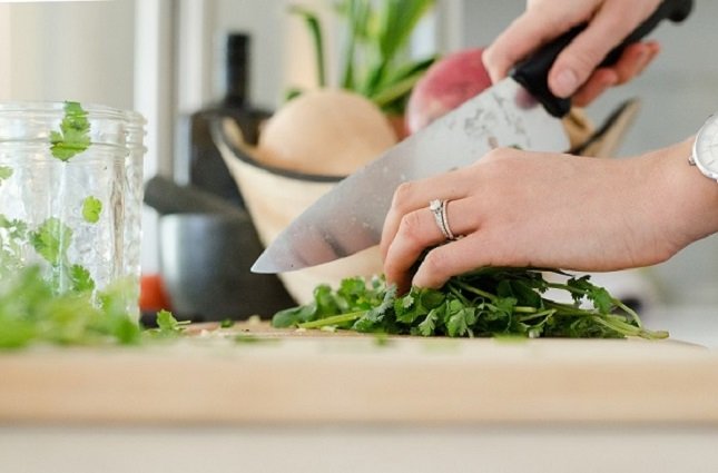 Hände einer Frau, die mit großem Küchenmesser Petersilie schneiden