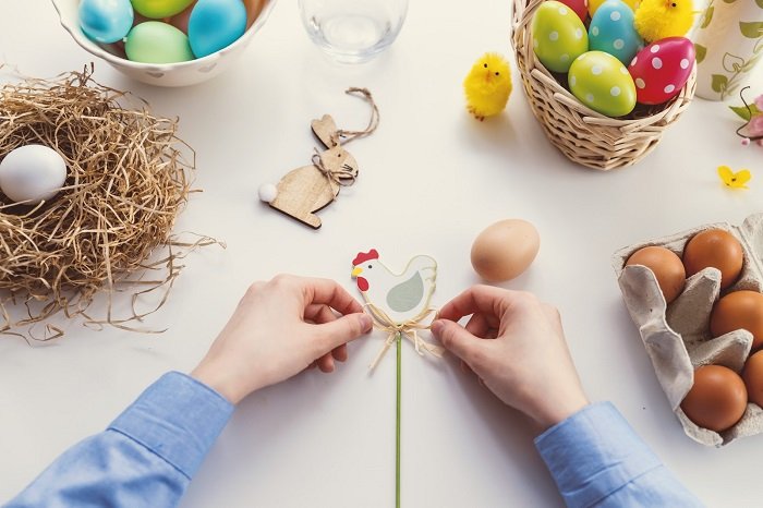 Person bastelt mit Stroh und Osterkorb an Dekoration zwischen bunten Ostereiern