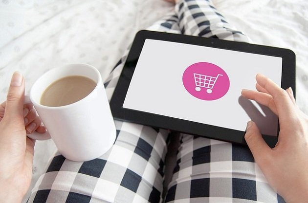 Person in Pyjama mit Tablet und einer Tasse Kaffee in der Hand