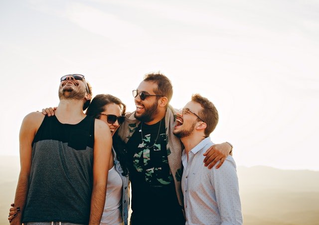 Eine Gruppe von vier Freunden umarmen sich lachend und haben Spaß