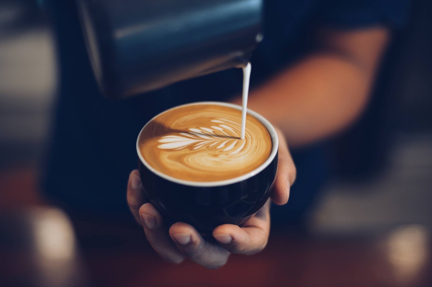 Personne servant une tasse de café avec mousse blanche