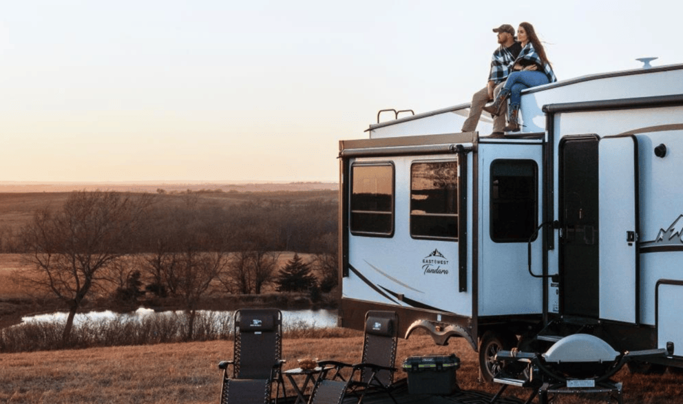 couple sitting on rv next to a lake