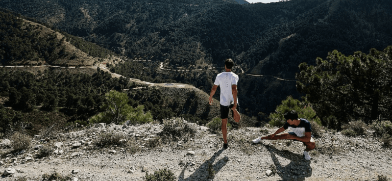 Two men stretching on a mountain trail wearing Castore sportswear