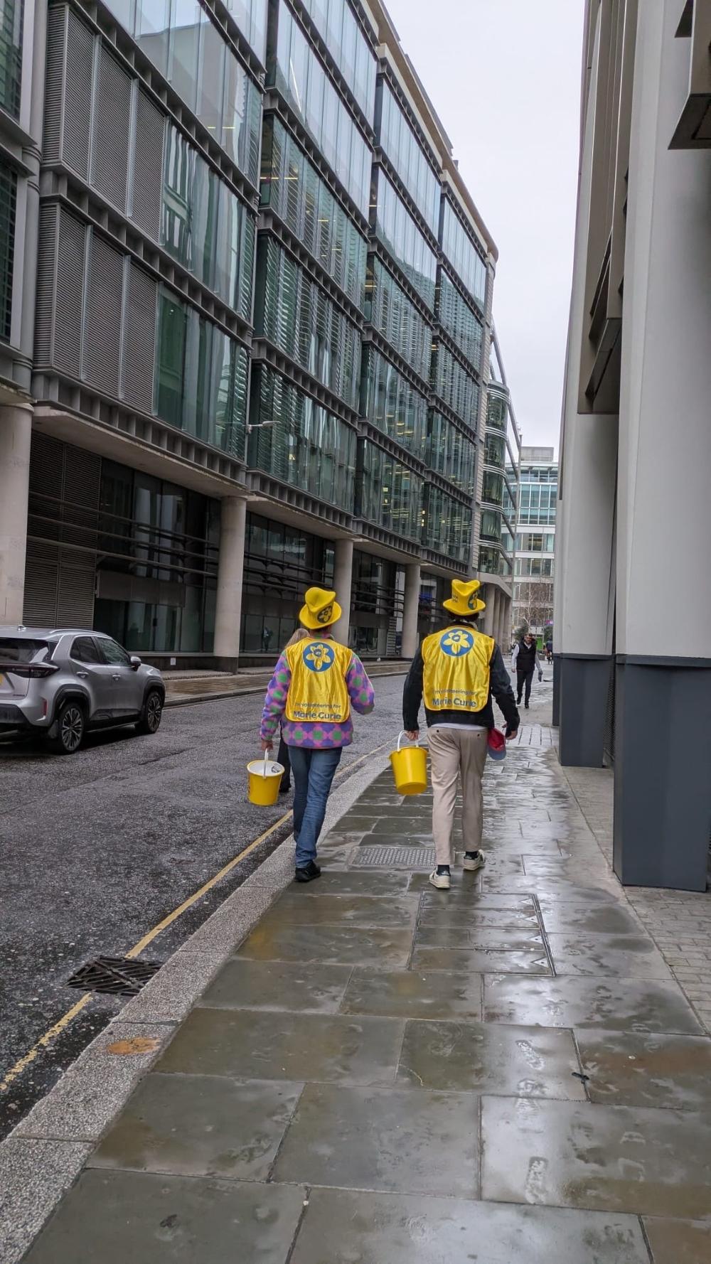 People walking on a rainy street with Marie Curie bibs and large hats