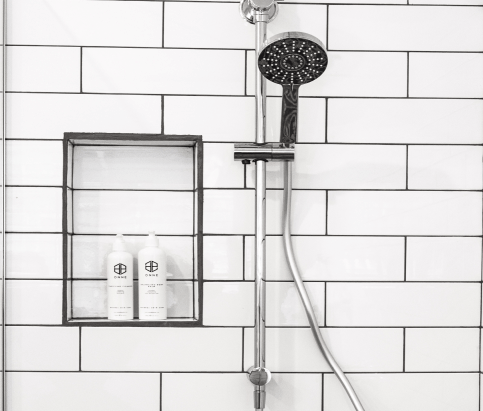 Shower head and body wash against a white tiled wall