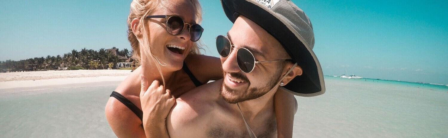 Couple on a beach image showing a woman hugging a man from behind in an exotic location