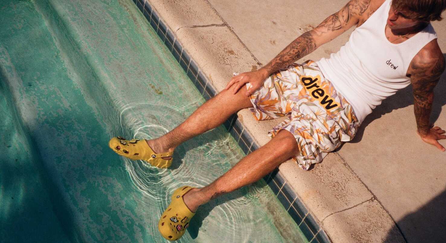 Crocs deals page image - Man wearing a t-shirt and shorts with his cros wearing feet in a pool
