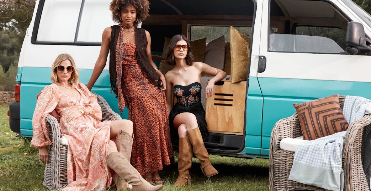 Debenhams summer looks banner showing three women in warm weather outfits outside of a camper van with rattan chairs