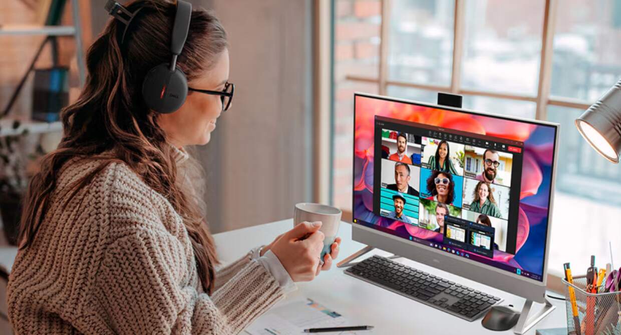 Dell deals page image featuring a smiling woman sitting at a desk on a laptop video call. The woman is holding a mug and has headphones on