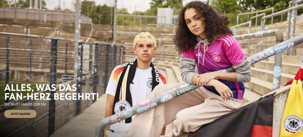 Zwei junge Menschen im DFB Heim- und Auslands-Trikot, Fan-Schal auf leerer Zuschauertribüne