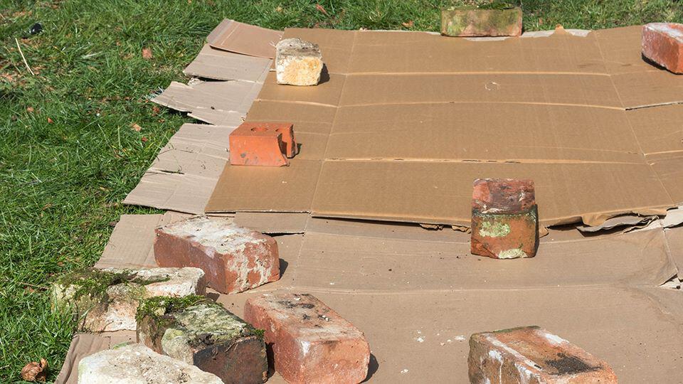 cardboard on grass being held down by brick and old glass jars