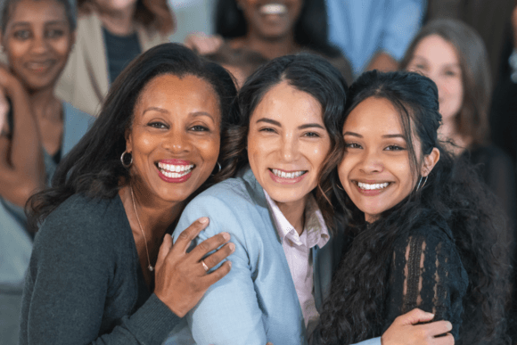 Three professional women posing in front of other women