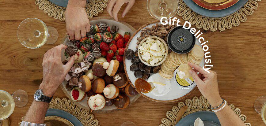 Edible Blooms deals page image showing two people tucking into food on two plates, with the text &apos;gift deliciously&apos; overlaid