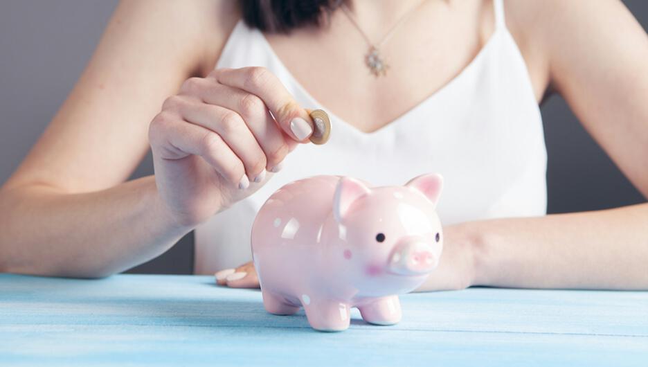 Close up of a woman putting a coin in a piggy bank