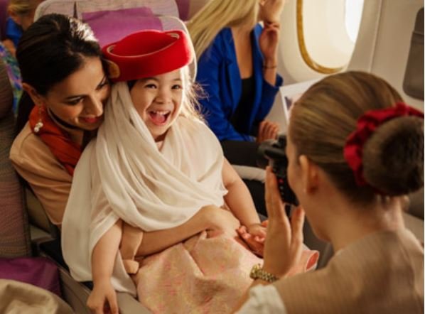 Kind in Emirates-Flugbegleiter-Uniform lacht auf Schoß der Mutter im Flugzeug