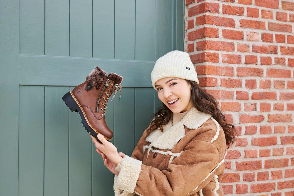femme brune avec un bonnet tenant une bottine Rieker du bout des doigts
