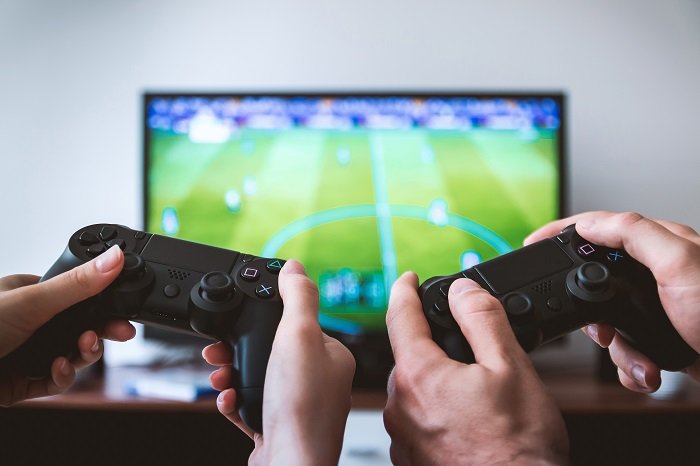 Zwei Freunde spielen Fifa auf der Playstation mit Controllern im Vordergrund