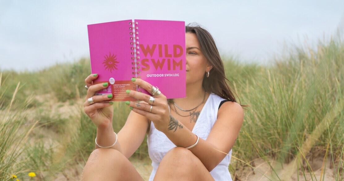 Good Tuesday offers page image featuring a women reading a bright pink note book in a beach setting