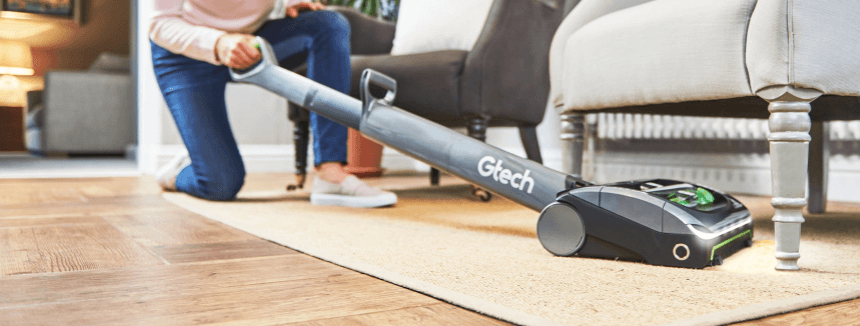 Gtech – Woman using an upright vacuum cleaner underneath the sofa