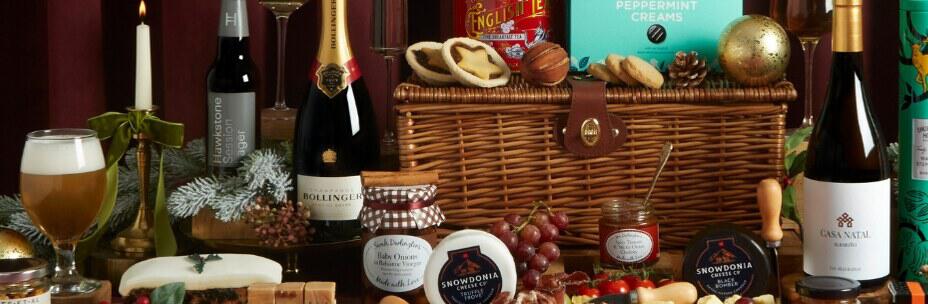 Hampers.com Christmas hamper banner featuring a selection of food and drink next to basket, including Bollinger, jam and fudge