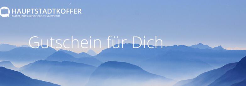 "Hauptstadtkoffer Gutschein für dich" über blau erscheinenden Gipfeln