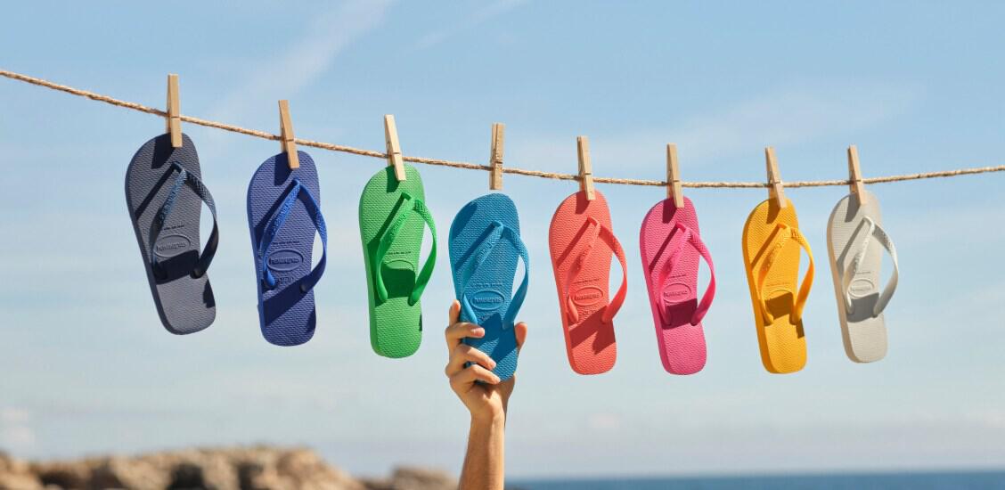 Havaianas deals page banner featuring 8 differently coloured sandals on a washing line with a hand grabbing the blue one
