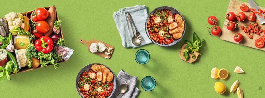 Différents fruits, légumes et plats colorés sur une table verte avec couverts et vaisselle