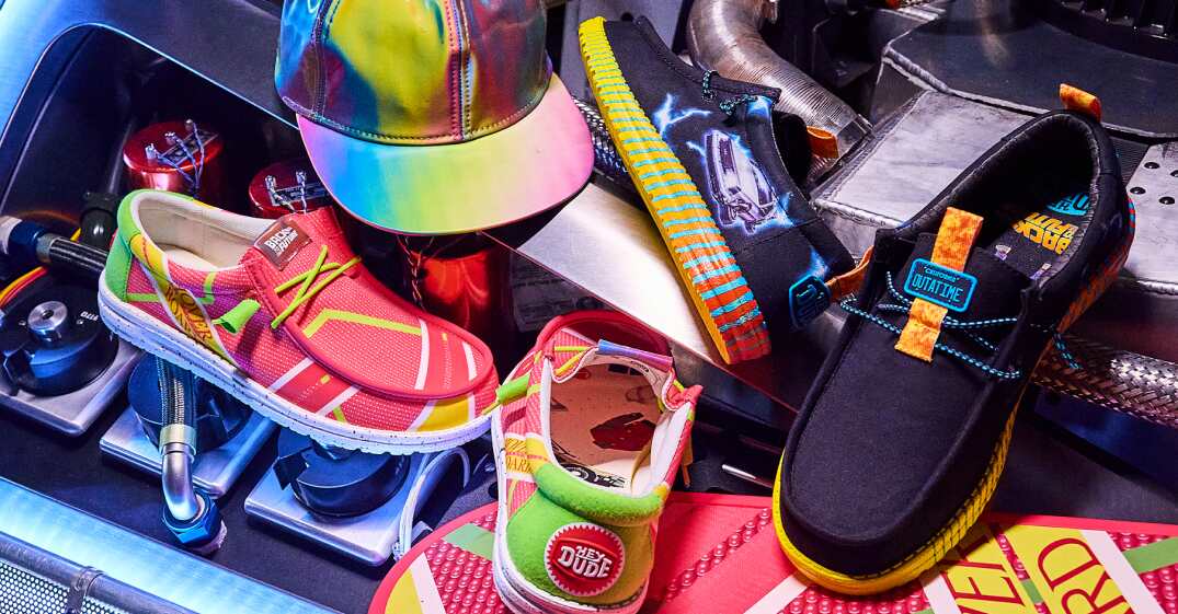 HEYDUDE deals page image featuring shoes from the Back to the Future movie collection, next to hoverboard and cap props from the films