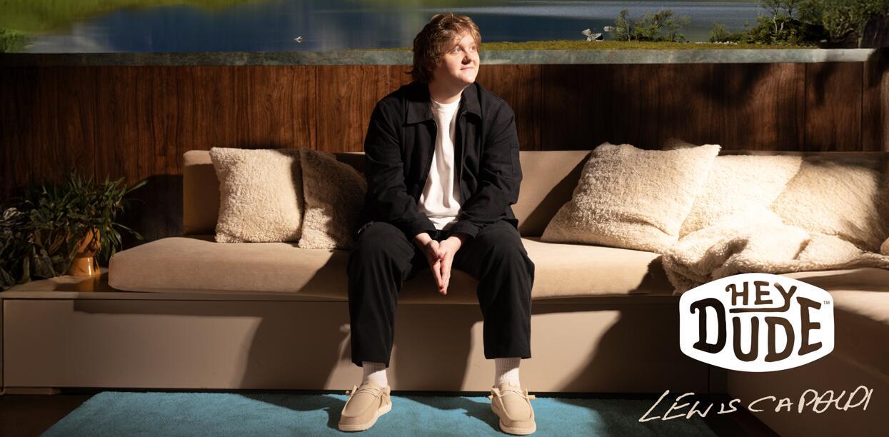 HEYDUDE savings page image featuring Lewis Capaldi sitting on a sofa wearing HEYDUDE shoes