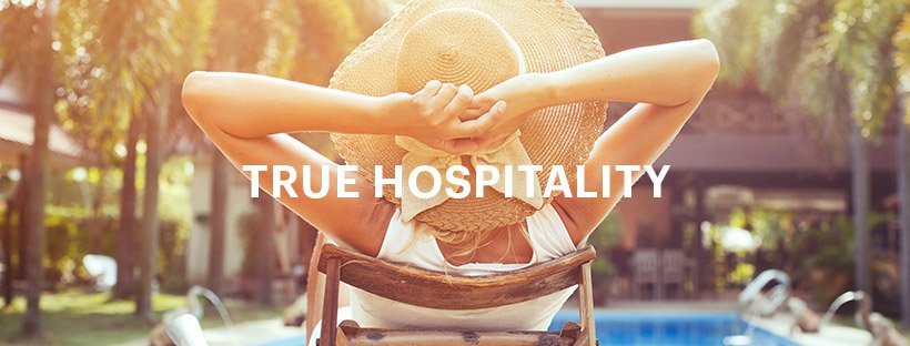 Woman relaxing on a sun lounger in front of a pool. Text reads: True Hospitality