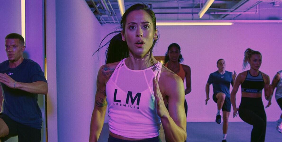 Les Mills how to save banner - Woman working out with other people in fitness gear under pink lighting