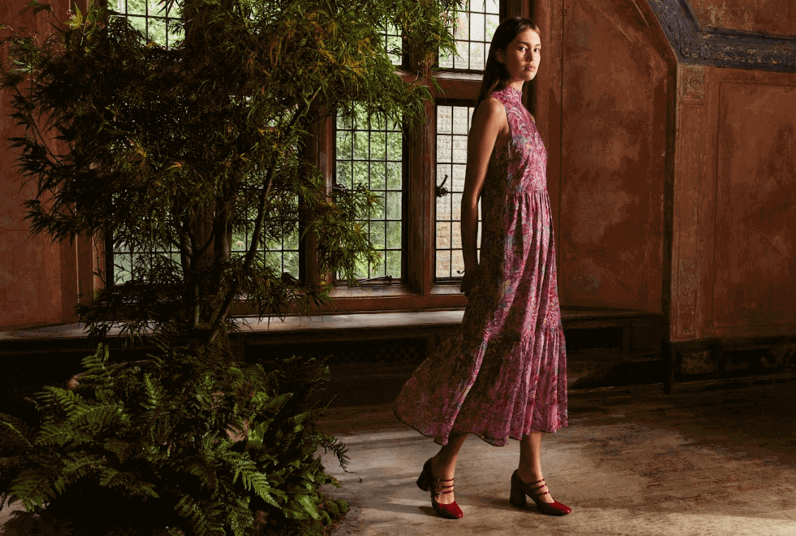 Liberty London discount codes page image - women in liberty print dress standing in a dark hall next to a large potted tree