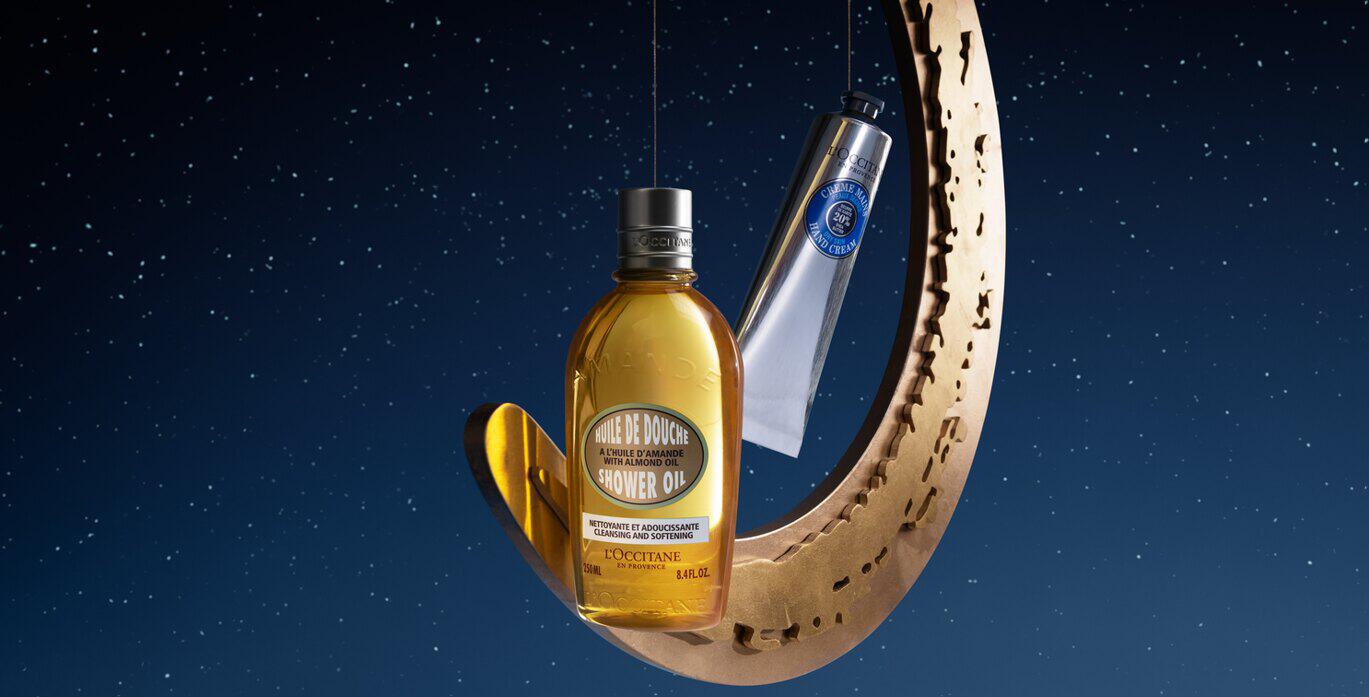 LOccitane Christmas savings tips image showing a branded shower gel and hand gream hanging alongside a gold festive decoration against blue backdrop