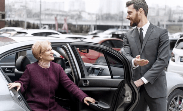 Luton Airport drop off image showing a man in a suit holding a car door open for a woman