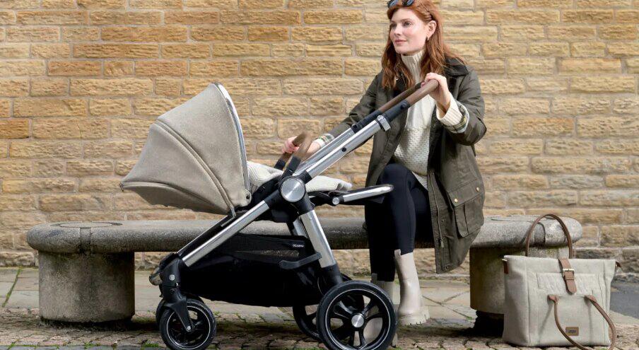 Mamas and Papas winter image - A woman wearing a coat sittiing on an outside bench with a pram