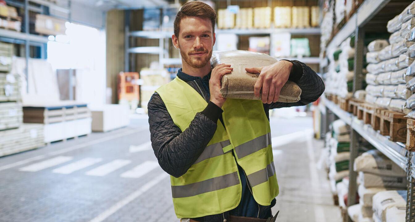 Materials Market offers page banner - A man in a high vis jacket carrying a bag on his shoulder in a warehouse