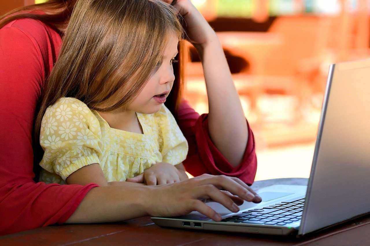 Petite fille sur les geneoux de sa maman devant un ordinateur