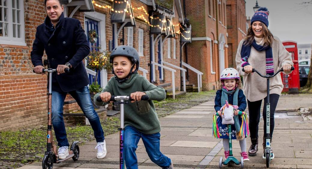 Micro Scooters savings guide image featuring a mum and dad with two children using micro scooters on a street