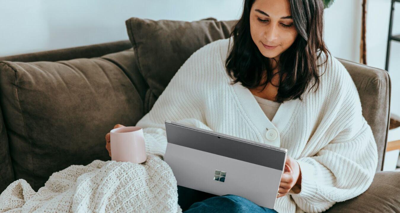 Microsoft savings tips image - A woman relaxing on a sofa with a Microsoft device