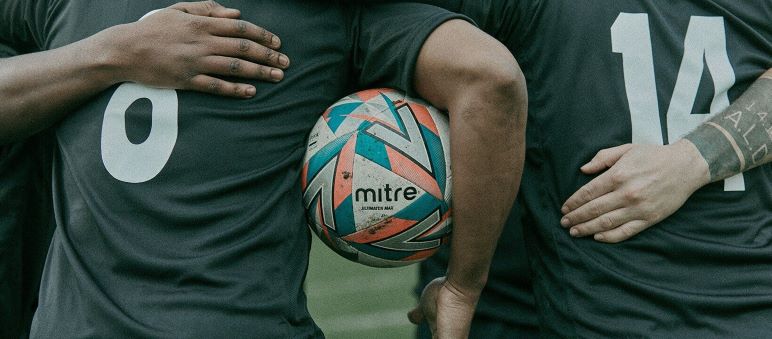 Footballer in football kit holding a Mitre football